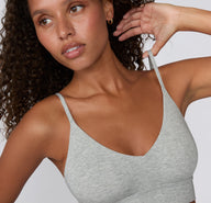 On a white studio backdrop, a model adjusts the strap of the Cloud Cotton Triangle Bralette in Heather Grey, showing the breathable cotton-modal fabric, low-profile seams, and flexible triangle silhouette.