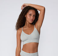 On a clean studio backdrop, a model poses in the Cloud Cotton Triangle Bralette in Heather Grey with the matching Cloud Cotton Bikini, showing the breathable cotton-modal fabric, wireless support, and low-profile silhouette.