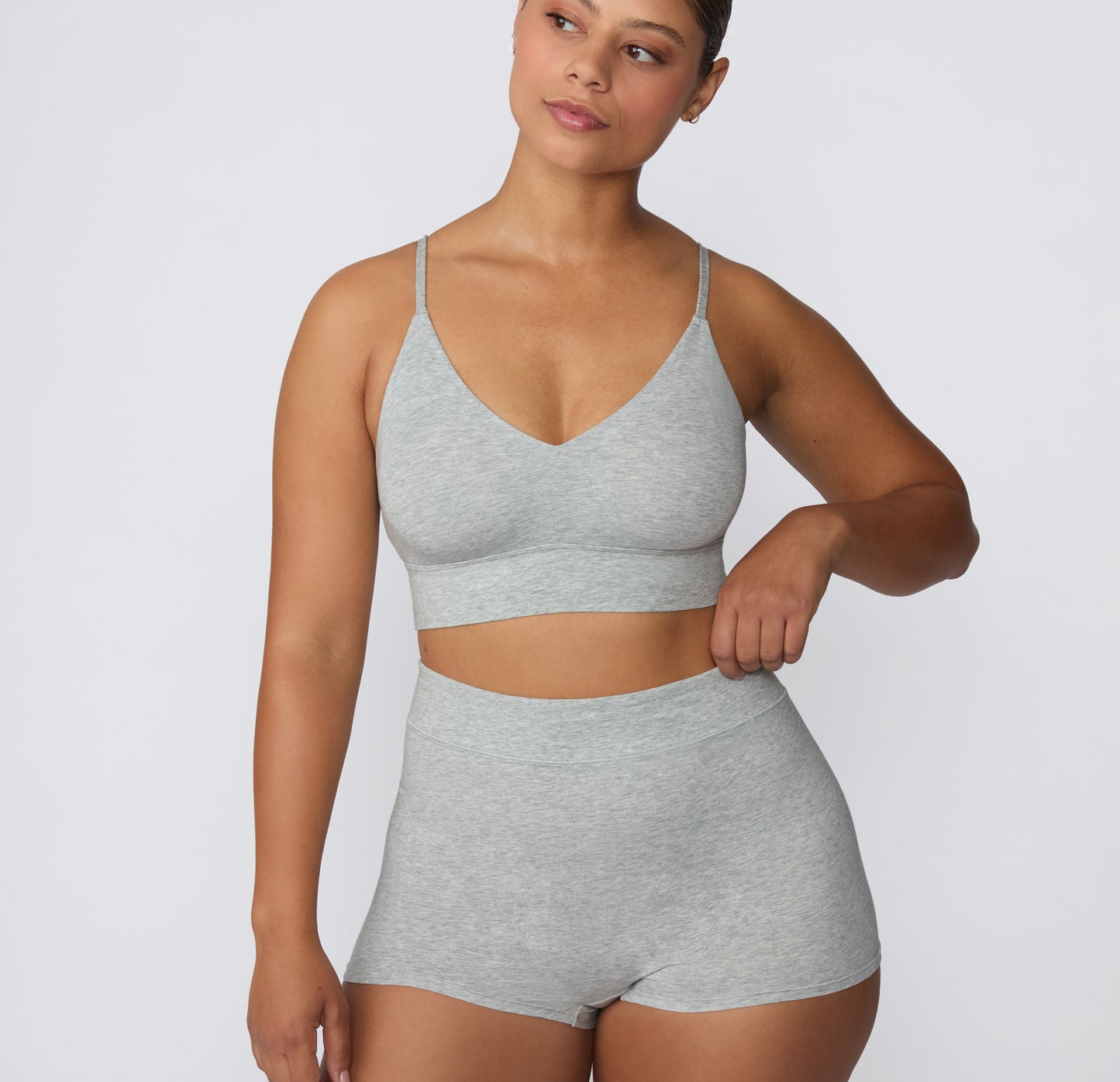 On a clean studio backdrop, a model wears the Cloud Cotton Triangle Bralette in Heather Grey with matching Cloud Cotton shorts, showing the wireless triangle silhouette, thin adjustable straps, and soft longline underband.