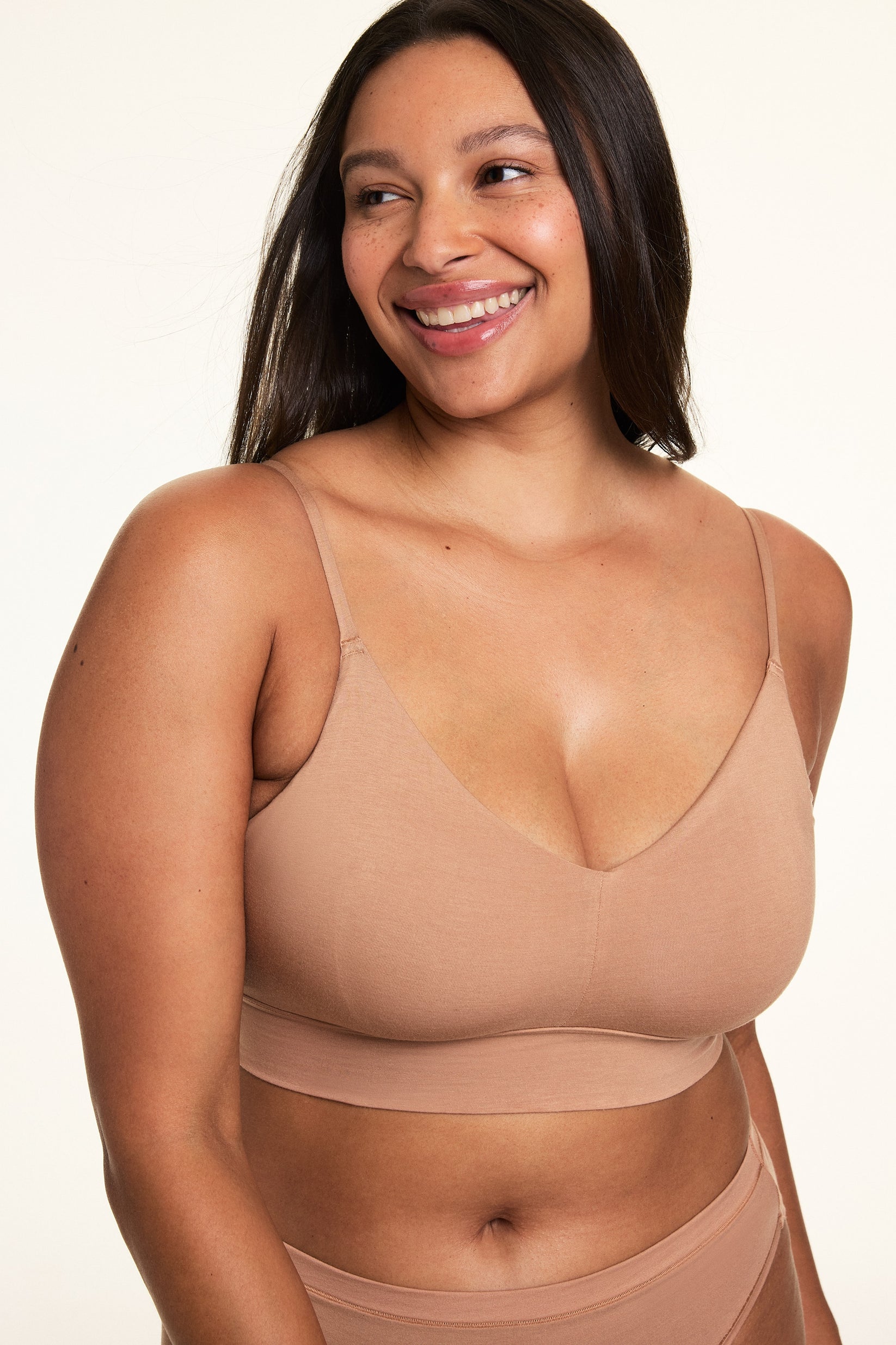 In a softly lit studio, Alana wears the Cloud Cotton Triangle Bralette in Dune with matching Cloud Cotton bottoms. The bralette features a deep V neckline, thin adjustable straps, and soft cotton modal fabric designed for lightweight everyday comfort.  