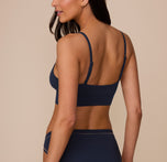 Back view of Marcela wearing the Cloud Cotton Triangle Bralette in Midnight. The low v-neck neckline and thin adjustable straps are emphasized. 