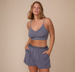 Sonnie poses with both her hands in her pockets, wearing the Cloud Cotton Triangle Bralette and Cloud Cotton Pajama Shorts in Slate. The image highlights the soft triangle shape and smooth cotton finish. 