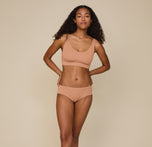 Full-body image of Zoe standing confidently with hands on hips, wearing the Cloud Cotton Scoop Bralette and Cloud Cotton Hiphugger in Dune, highlighting the soft, lightweight fabric and flattering fit designed for everyday comfort.