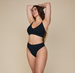 Summerlyn standing confidently with arms raised, wearing the Cloud Cotton Triangle Bralette and Cloud Cotton Highwaist Thong in Black, showcasing the soft, comfortable fit.
