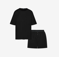 Flat lay of the Cloud Cotton Sleep Set in Black, featuring a short-sleeve tee with chest pocket and matching boxer-style sleep shorts. The shorts have a button fly and tonal waistband with a thin black stripe detail. Displayed against a white background for a clean, minimal presentation.