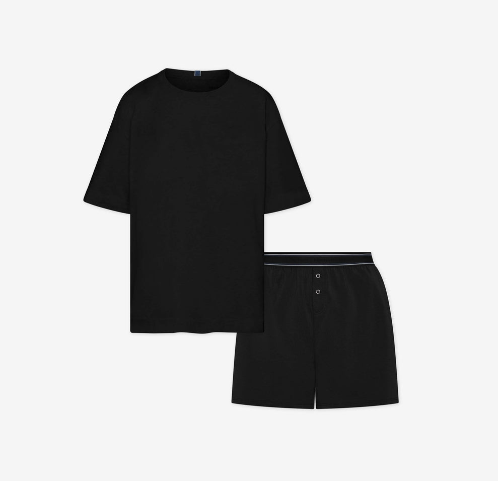 Flat lay of the Cloud Cotton Sleep Set in Black, featuring a short-sleeve tee with chest pocket and matching boxer-style sleep shorts. The shorts have a button fly and tonal waistband with a thin black stripe detail. Displayed against a white background for a clean, minimal presentation.