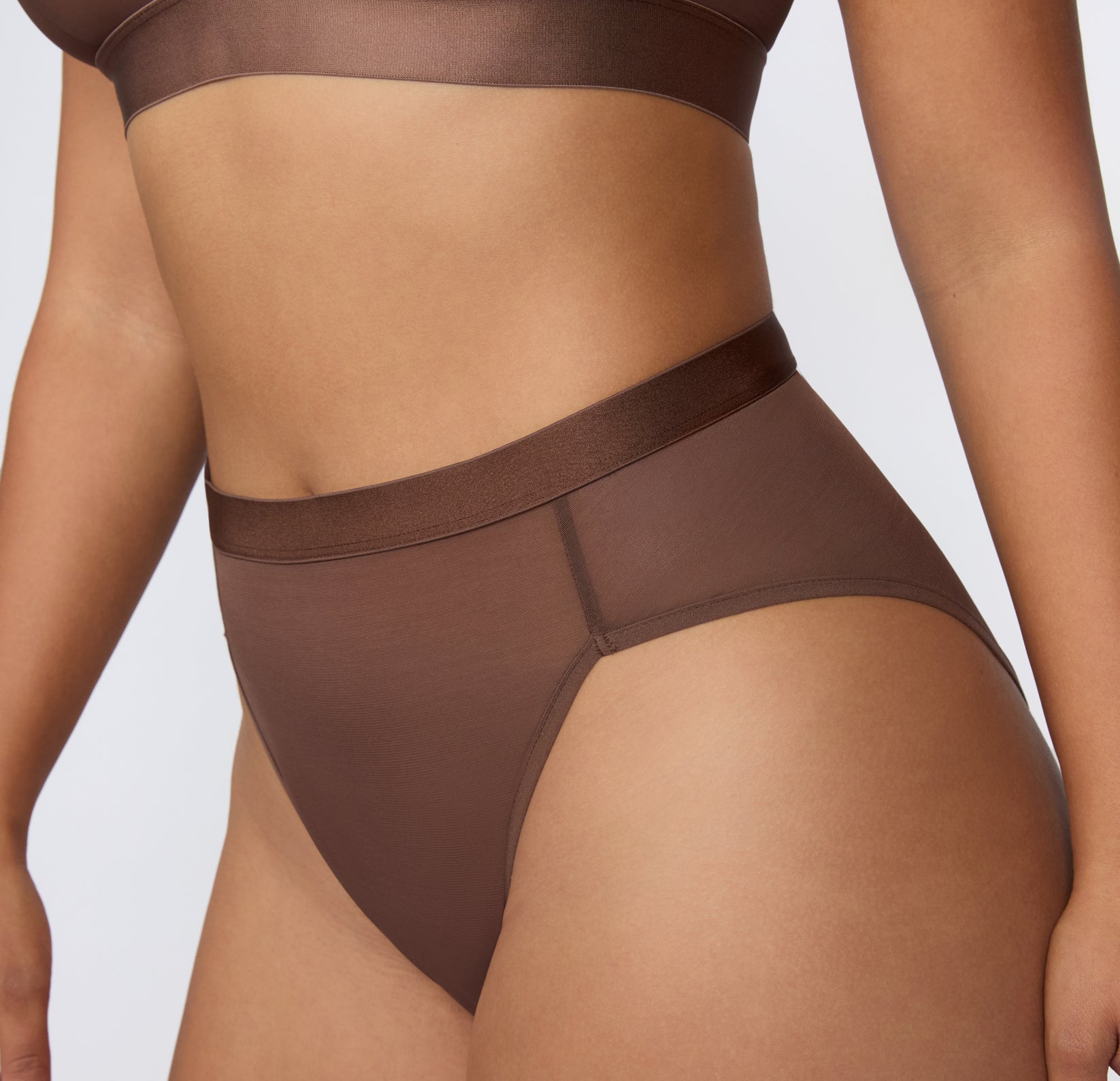 On a white studio backdrop, a close-up three-quarter view shows the ComfortMesh™ Highwaist in Cashmere worn with the matching bralette, highlighting the sheer mesh fabric, smooth waistband, and high-rise coverage.