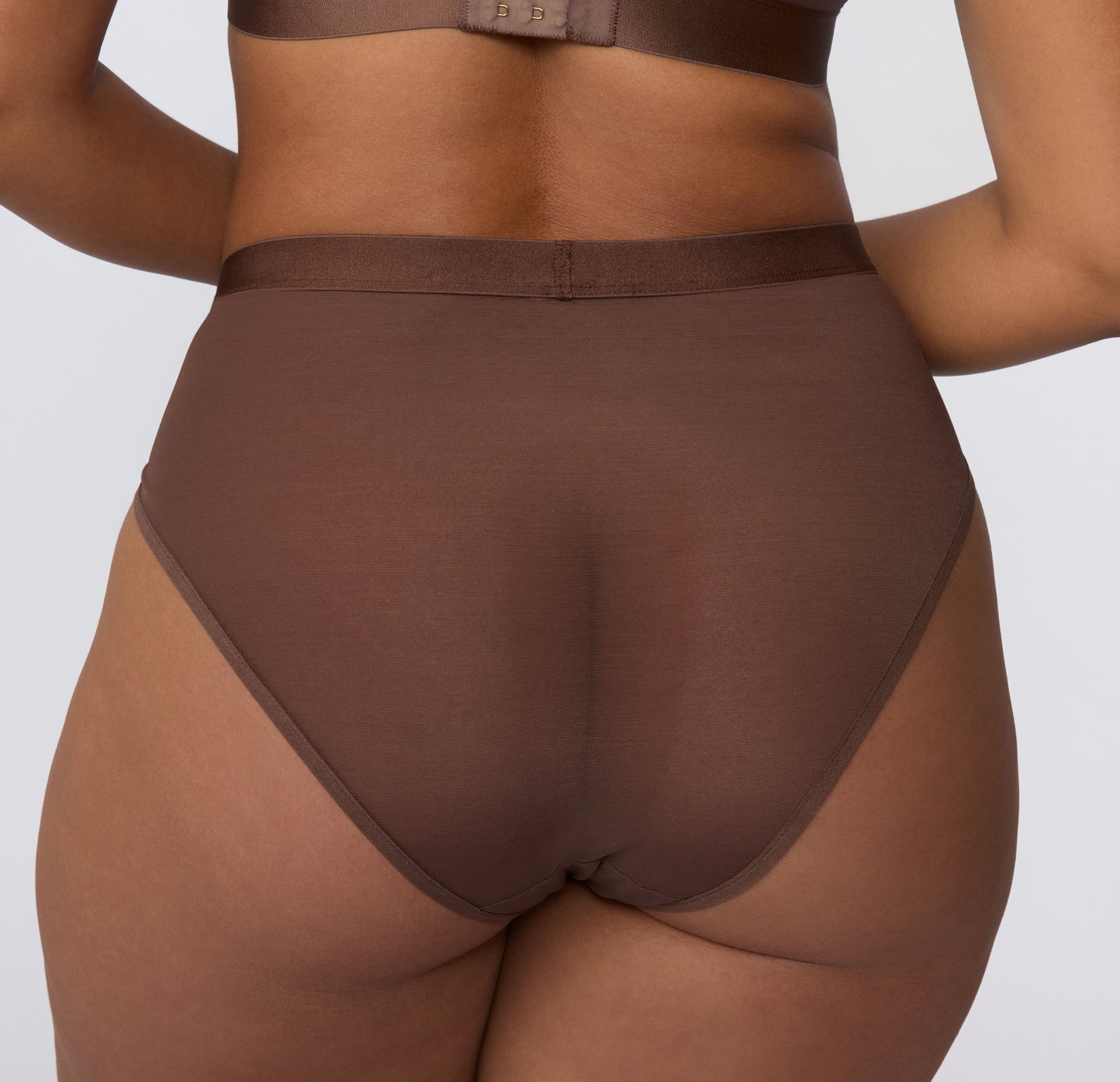 On a white studio backdrop, a back view shows the ComfortMesh™ Highwaist in Cashmere worn with the matching bralette, highlighting the sheer mesh back panel and smooth, high-rise waistband.