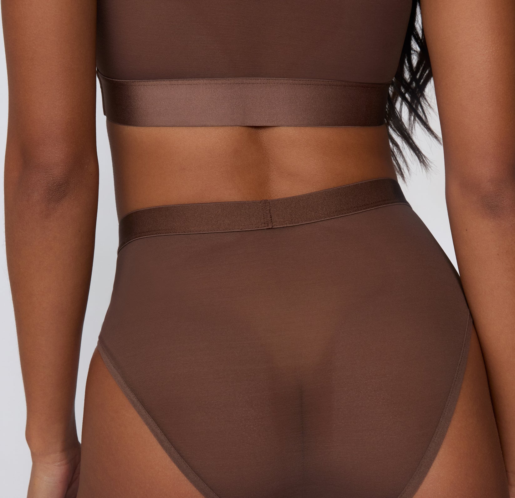 On a white studio backdrop, a back view shows the ComfortMesh™ Highwaist in Cashmere worn with the matching bralette, highlighting the sheer mesh fabric and smooth, high-rise waistband.