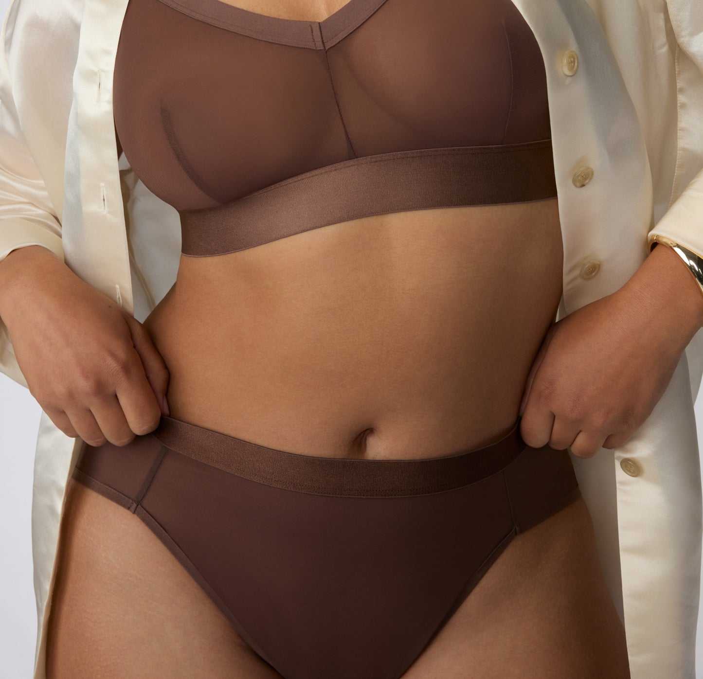 On a white studio backdrop, Amber wears the ComfortMesh™ Highwaist in Cashmere styled with an open button-down, shown in a front-facing view highlighting the sheer mesh fabric and smooth waistband.
