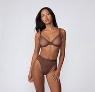 On a white studio backdrop, a model wears the ComfortMesh™ Plunge Bra in Cashmere Amber with matching underwear, shown from the front to highlight the sheer cups and supportive plunge shape.