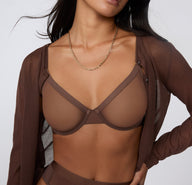 On a white studio backdrop, a model wears the ComfortMesh™ Plunge Bra in Cashmere Amber under a lightweight brown cardigan, showing the plunge front and soft, sheer mesh fabric.