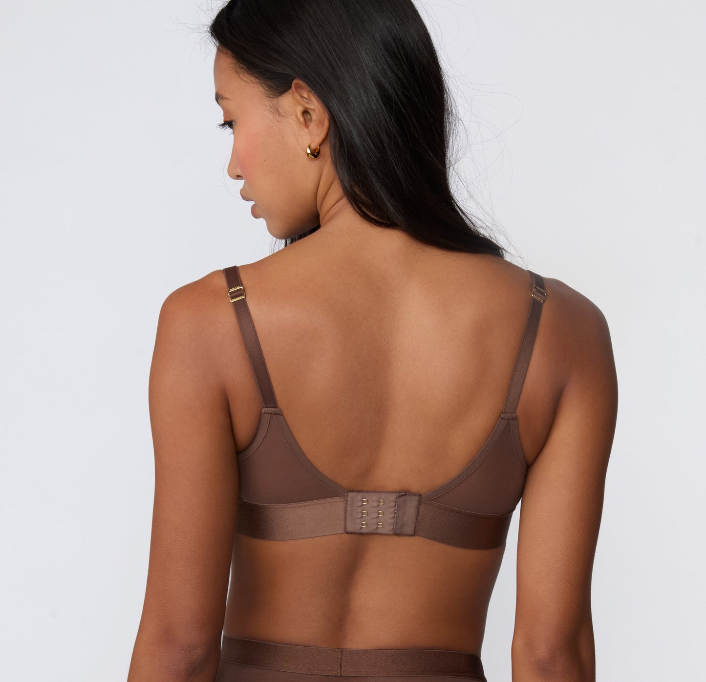 On a white studio backdrop, a back view shows the ComfortMesh™ Plunge Bra in Cashmere Amber, highlighting the adjustable straps, hook-and-eye ballet back, and wide supportive band.