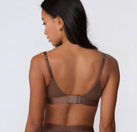 On a white studio backdrop, a back view shows the ComfortMesh™ Plunge Bra in Cashmere Amber, highlighting the adjustable straps, hook-and-eye ballet back, and wide supportive band.