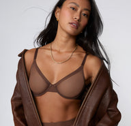 On a white studio backdrop, a model wears the ComfortMesh™ Plunge Bra in Cashmere Amber under an open leather jacket, showing the plunging neckline and sheer mesh construction.