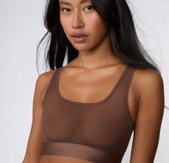 On a white studio backdrop, a close-up view shows Amber wearing the ComfortMesh™ Scoop Bralette in Cashmere, focusing on the scoop neckline, sheer mesh cups, and smooth microfiber band.