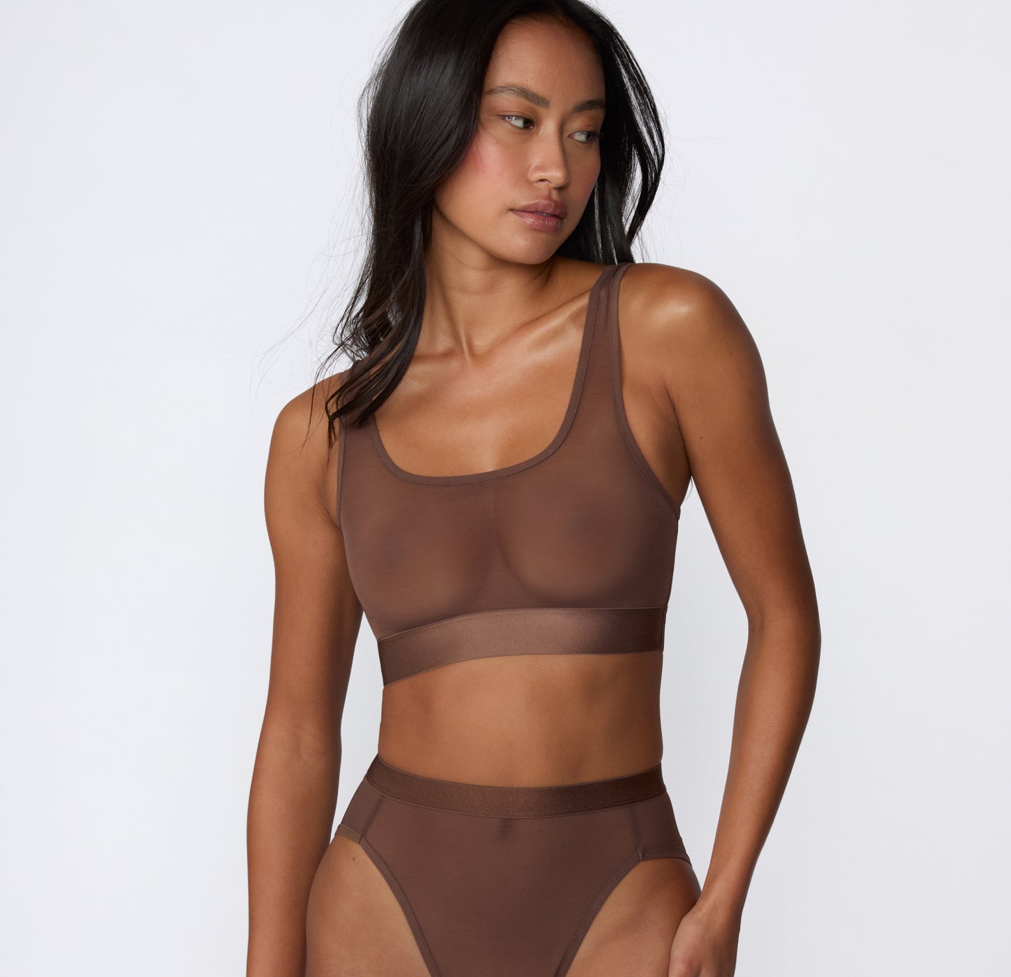 On a white studio backdrop, a three-quarter side view shows Amber wearing the ComfortMesh™ Scoop Bralette in Cashmere, highlighting the sheer mesh fabric, scoop neckline, and smooth wide band.