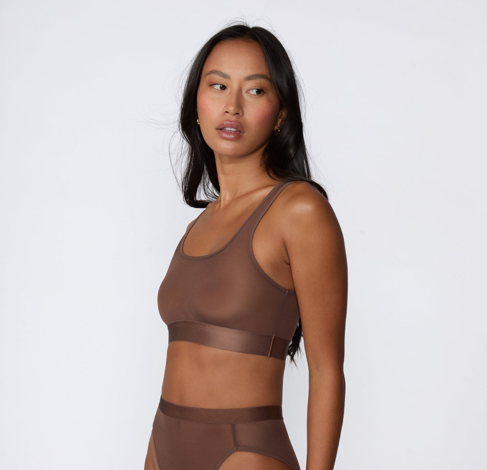 On a white studio backdrop, a side view shows Amber wearing the ComfortMesh™ Scoop Bralette in Cashmere with matching bottoms, highlighting the scoop neckline, sheer mesh fabric, and wide supportive band.