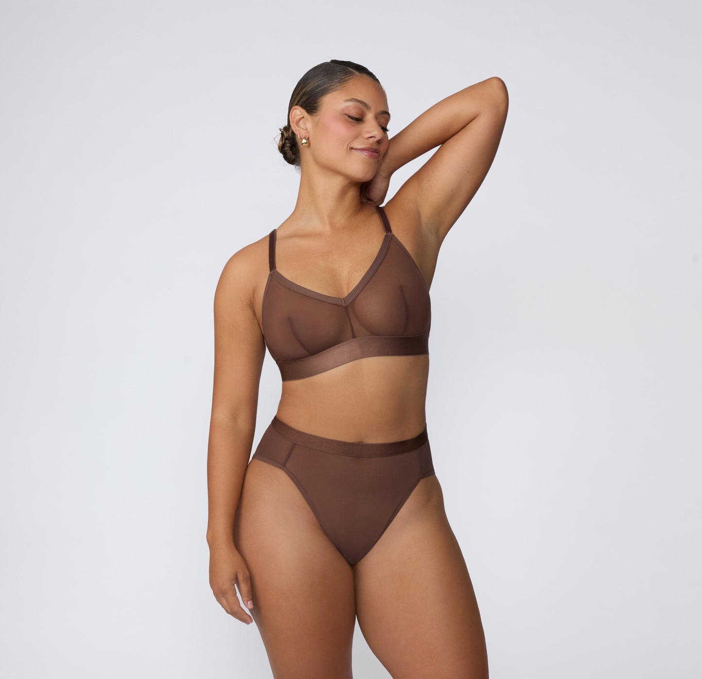 On a white studio backdrop, India wears the ComfortMesh™ Triangle Bralette in Cashmere with matching bottoms, shown in a full-body view highlighting the sheer mesh fabric, V-neckline, adjustable straps, and wide supportive band.