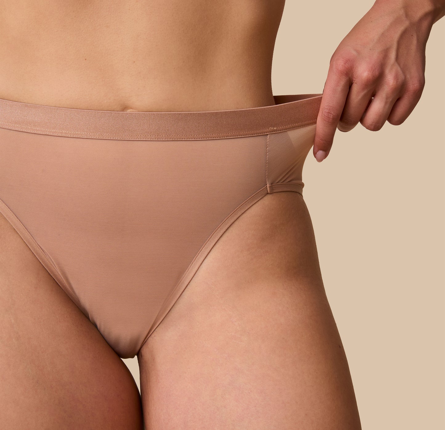 A close-up showcasing the stretchable ComfortMesh™ waistband of the taupe highwaist briefs, with the model gently pulling the fabric to highlight its flexibility and softness.