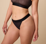 Emersyn poses wearing the ComfortMesh Thong in Black. The wide, comfortable waistband and sheer, stretchy fabric are emphasized. sizing: Emersyn wears a size Medium
