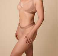 A profile view of a model wearing the ComfortMesh™ Thong in Taupe, emphasizing the high-leg cut and soft waistband that sits smoothly against the skin for a comfortable fit. 