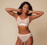 Ally posing with her hands behind her head, wearing the ComfortMesh™ Triangle Bralette in Pearl paired with matching bottoms. The sheer and smooth fabric highlights a modern design.