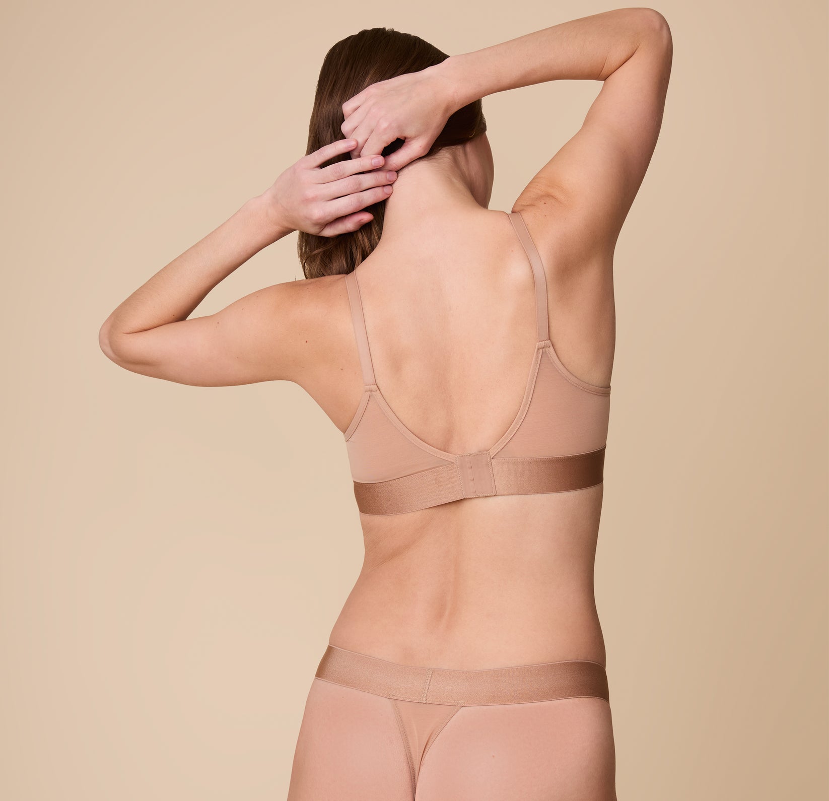 A back view of Gracie with her hands raised, showcasing the supportive band and minimalist design of the ComfortMesh™ Triangle Bralette in Taupe.