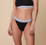 Close-up of model Gracie wearing the Harper Wilde Cloud Cotton Retro French Cut Bikini in Black. The high-cut bikini sits comfortably on the hips with a wide elastic waistband featuring a classic black and white stripe detailing. sizing: Gracie wears size Small