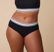 Close-up of India wearing the Cloud Cotton Retro Hiphugger in Black. The image highlights the thick elastic waistband with black and white stripes. The soft cotton fabric ensures a snug, comfortable fit. sizing: India wears size Large 