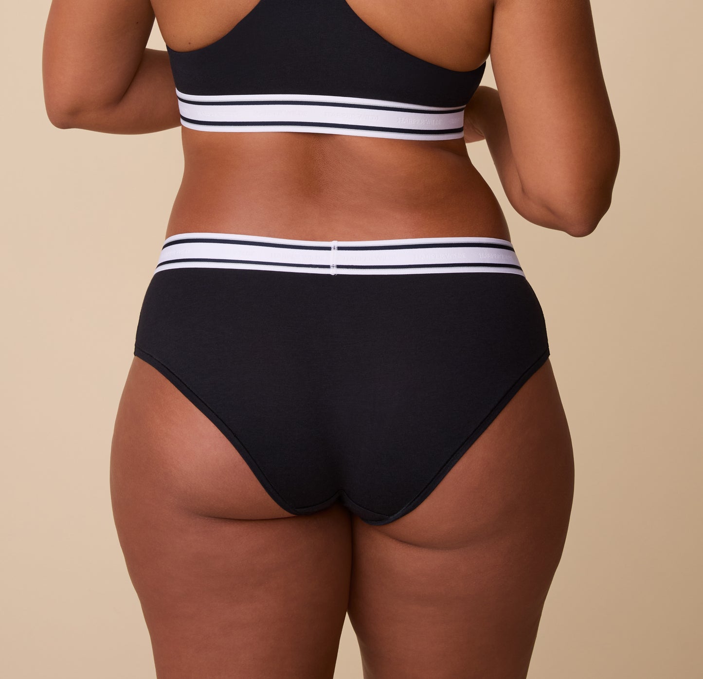 Back view of the Cloud Cotton Retro Hiphugger in Black. India showcases the full-coverage back with a smooth fit, emphasizing the soft fabric and supportive waistband.