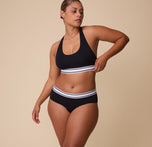 Full-body shot of India wearing the Cloud Cotton Retro Hiphugger in Black with the matching Racerback Bralette. She poses naturally, showcasing the sporty-chic style and comfort of the set.