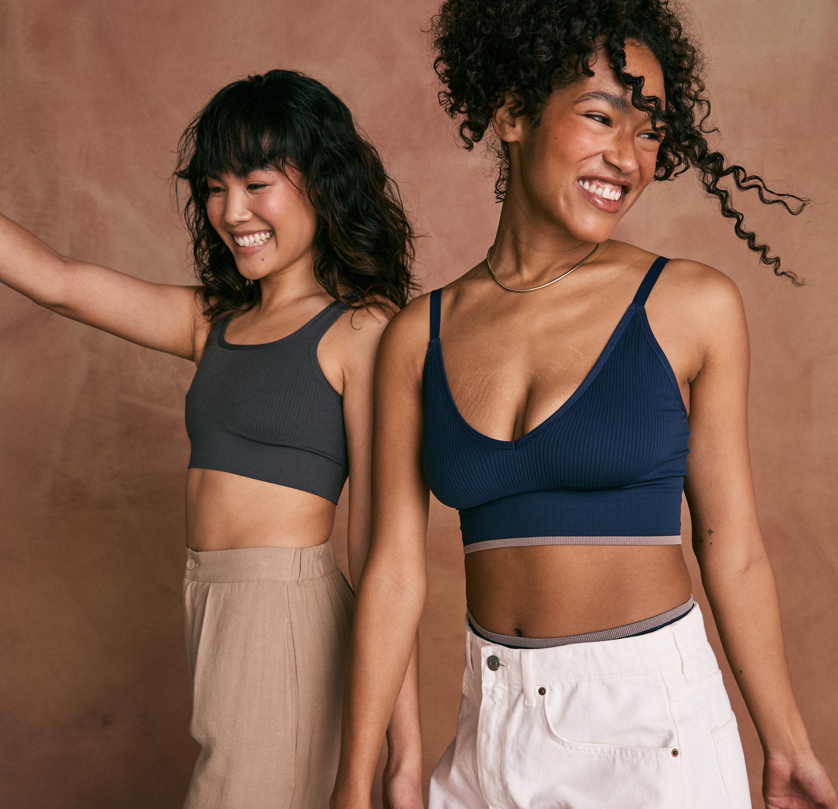 Two models standing next to each other wearing the Lounge Rib Scoop Bralette and the Lounge Rib Triangle Bralette.