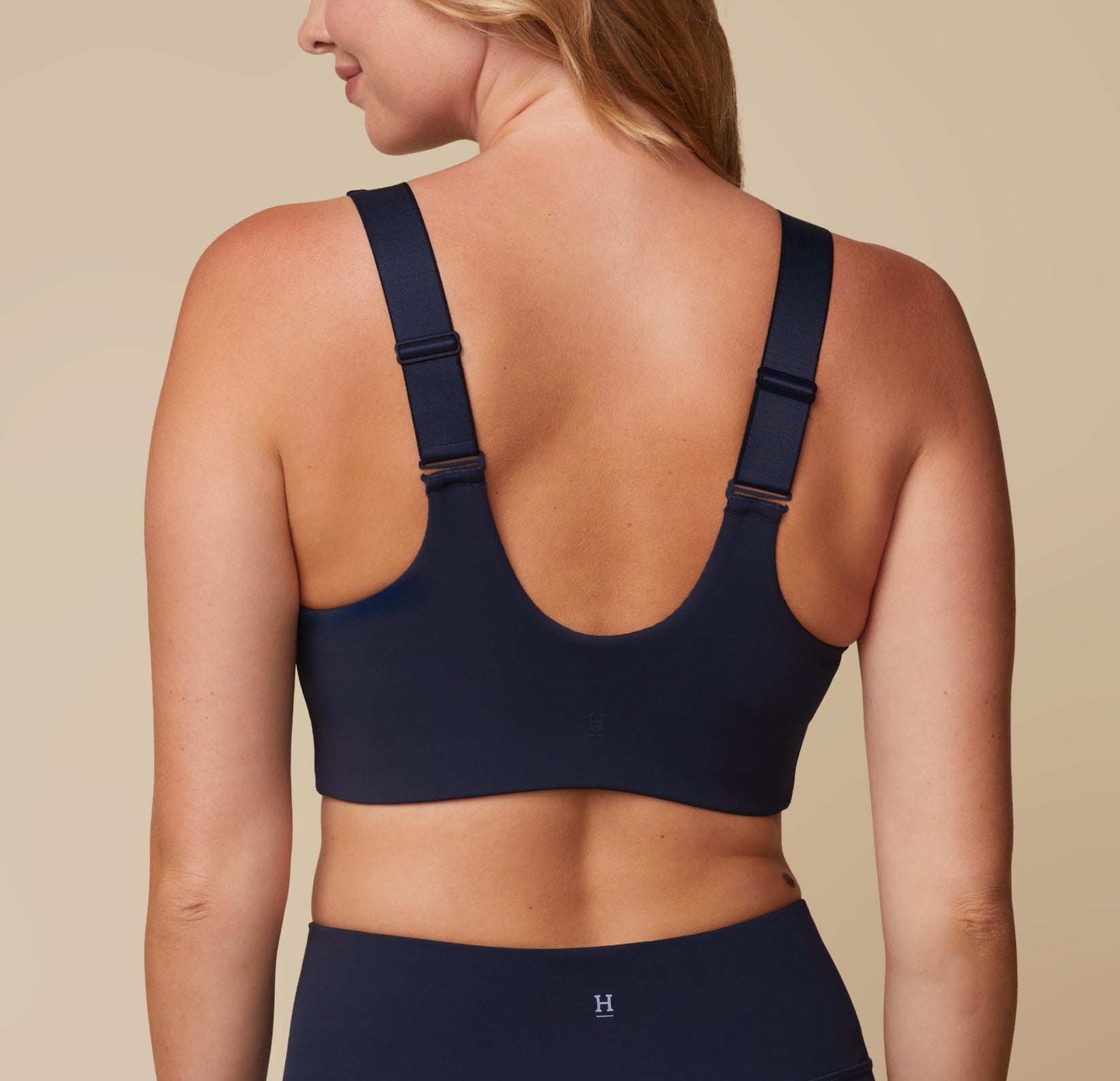 Back view of Megan wearing the Flex Convertible Sports Bra in Ink. The thick convertible straps and wide, comfortable band are emphasized. sizing: Megan wears size Medium