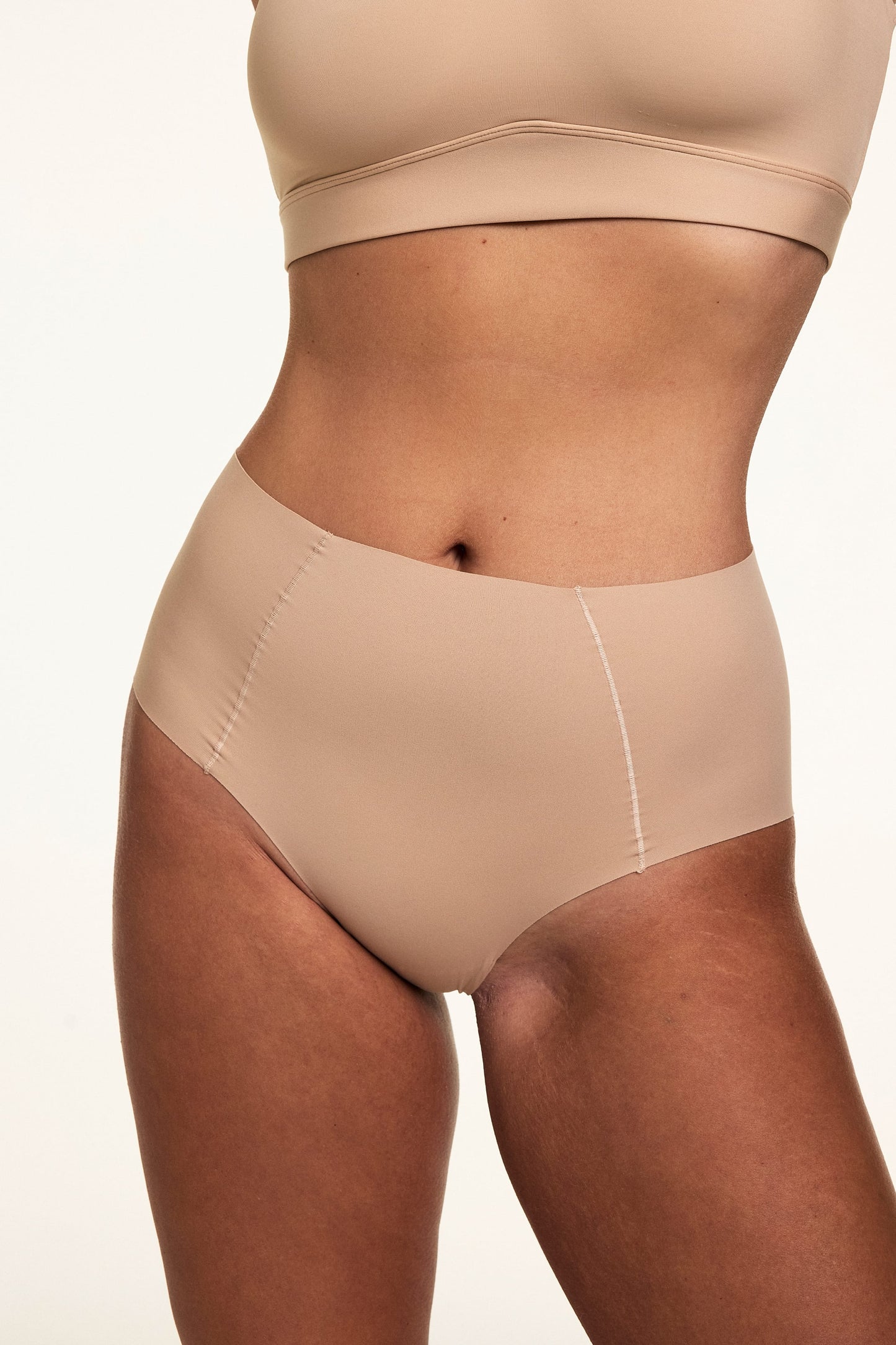 In a close-up studio shot, Sonnie wears the No Show Highwaist Brief in Beige with the Bliss Scoop Adjustable Bra in Beige, showing the high-rise silhouette and raw-edge sides.