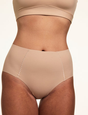 In a front-facing studio portrait, Sonnie wears the No Show Highwaist Brief in Beige, featuring smooth microfiber fabric, a high-rise fit, and no-show edges under clothing. sizing: Sonnie wears size Large