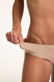 In a close-up studio shot, Gianna stretches the waistband of the Invisible No Show Hiphugger in Beige, showing the soft stretch fabric and flexible fit.