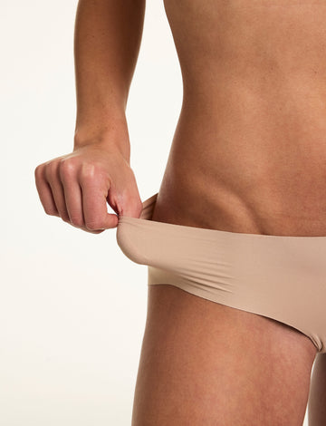 In a close-up studio shot, Gianna stretches the waistband of the Invisible No Show Hiphugger in Beige, showing the soft stretch fabric and flexible fit.