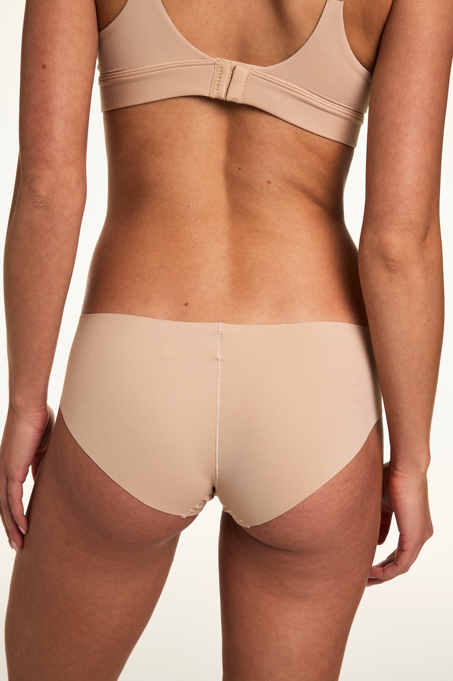 From the back on a white studio backdrop, Gianna wears the Invisible No Show Hiphugger in Beige, showing the smooth waistband and no-show finish.