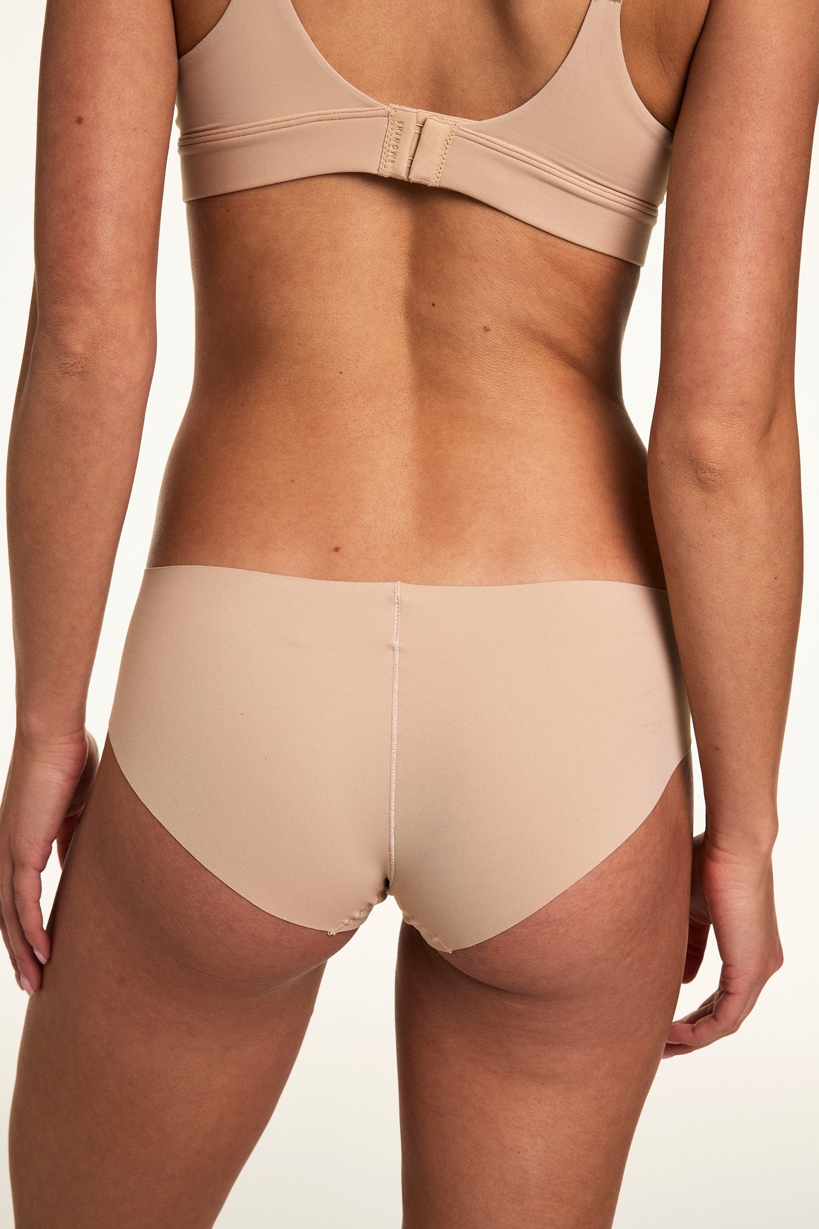 From the back on a white studio backdrop, Gianna wears the Invisible No Show Hiphugger in Beige, showing the smooth waistband and no-show finish.