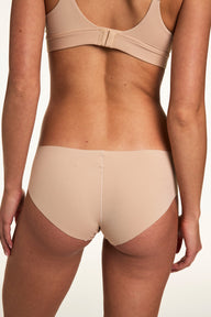 From the back on a white studio backdrop, Gianna wears the Invisible No Show Hiphugger in Beige, showing the smooth waistband and no-show finish.