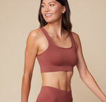 Anna is captured at a slight angle, smiling, while wearing the Lounge Rib Scoop Bralette and Lounge Rib Boyshort in Clay.