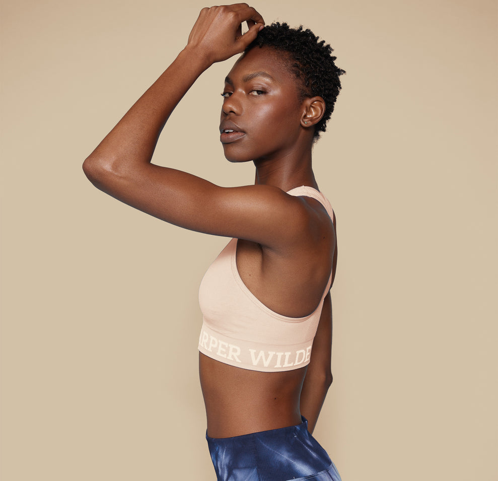 Side profile of model Mariah in the Move Sports Bra in Beige, with one hand resting on her head, emphasizing the comfortable fit and supportive design.
