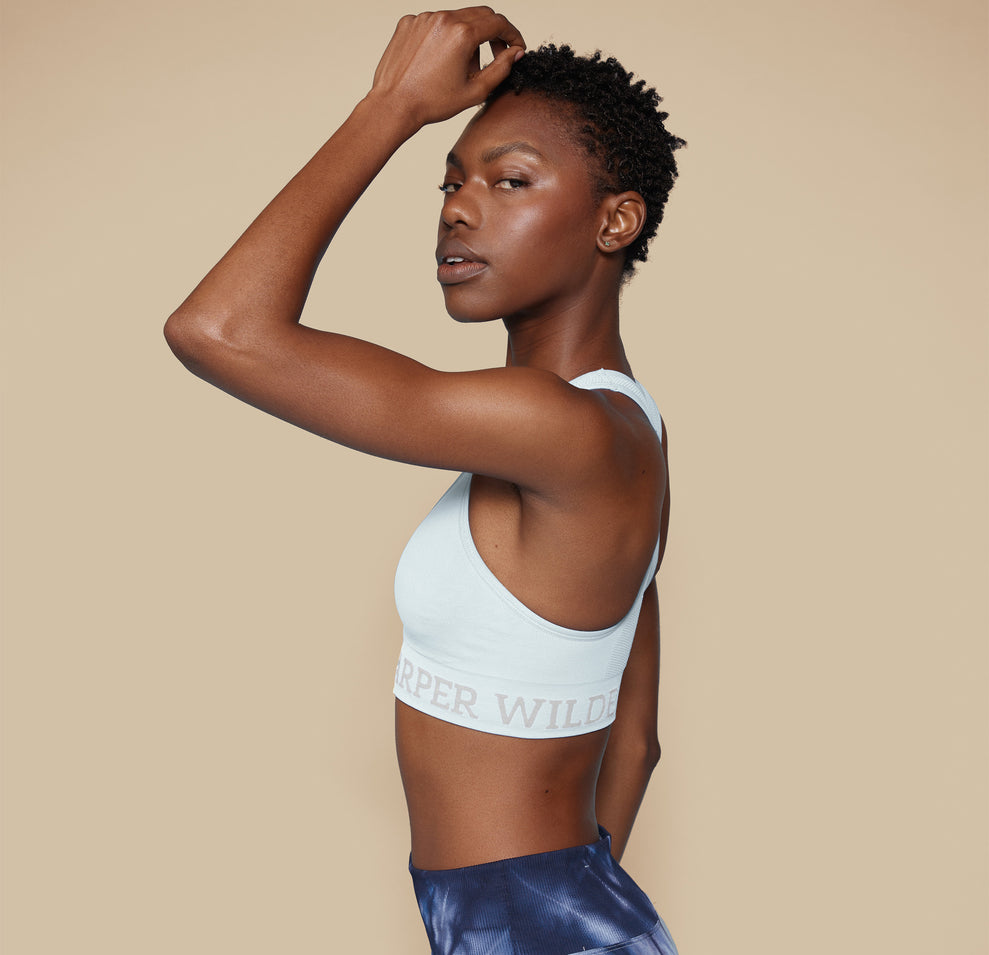 Side profile of model Mariah in the Move Sports Bra in Ice, with one hand resting on her head, emphasizing the comfortable fit and supportive design.