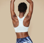 Back view of model Mariah in the Move Sports Bra in Ice, with both arms raised, displaying the racerback style.