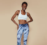 Full body shot of Mariah in the Move Sports Bra in Ice, paired with blue tie-dye leggings, standing with hands on hips and smiling confidently.