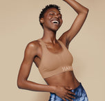 Model Mariah smiles brightly while wearing the Move Sports Bra in Tan, with one arm raised, showcasing the sporty fit and Harper Wilde logo on the band.