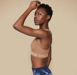 Side profile of model Mariah in the Move Sports Bra in Tan, with one hand resting on her head, emphasizing the comfortable fit and supportive design.