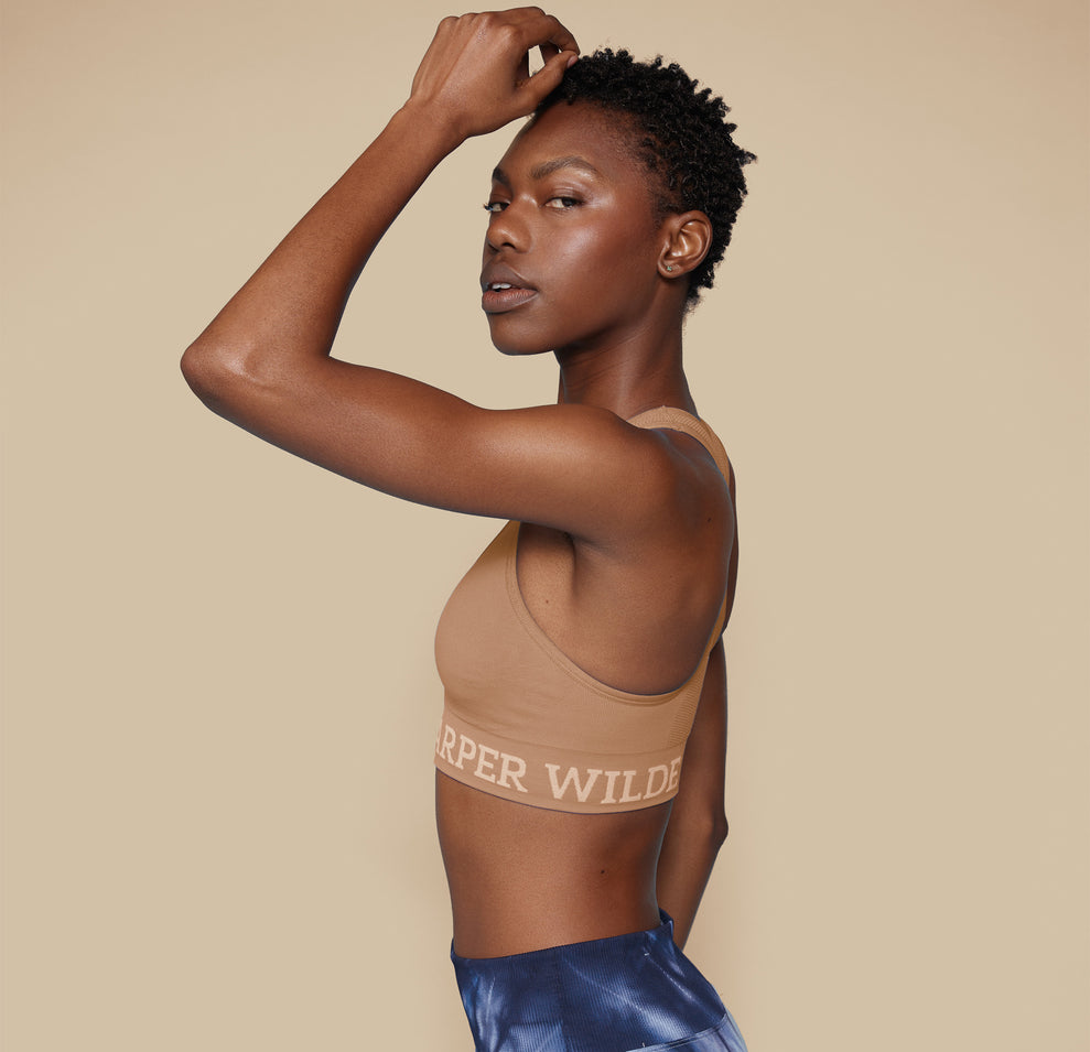 Side profile of model Mariah in the Move Sports Bra in Tan, with one hand resting on her head, emphasizing the comfortable fit and supportive design.