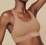 Close-up side view of Mariah wearing the Move Sports Bra in Tan, highlighting the scoop neckline and Harper Wilde logo on the band.